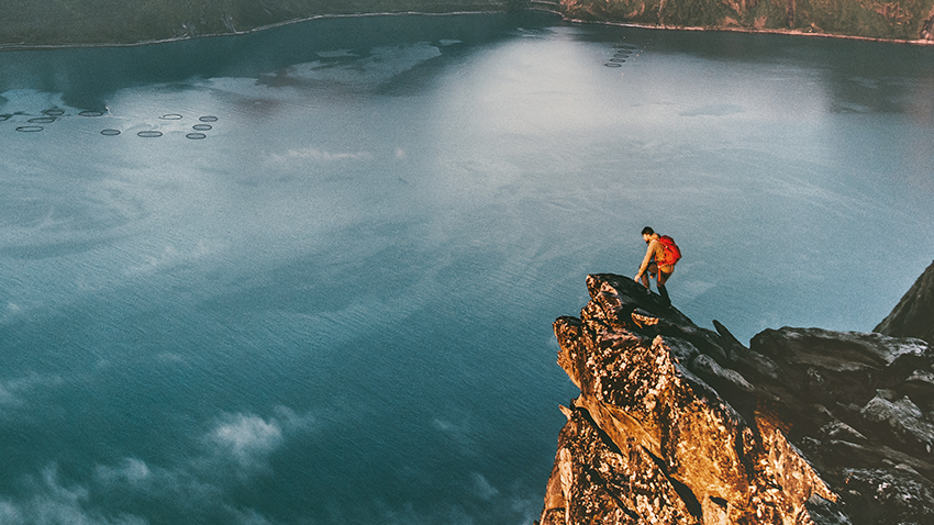 hiker reaching the peak of a mountaintop on a lake