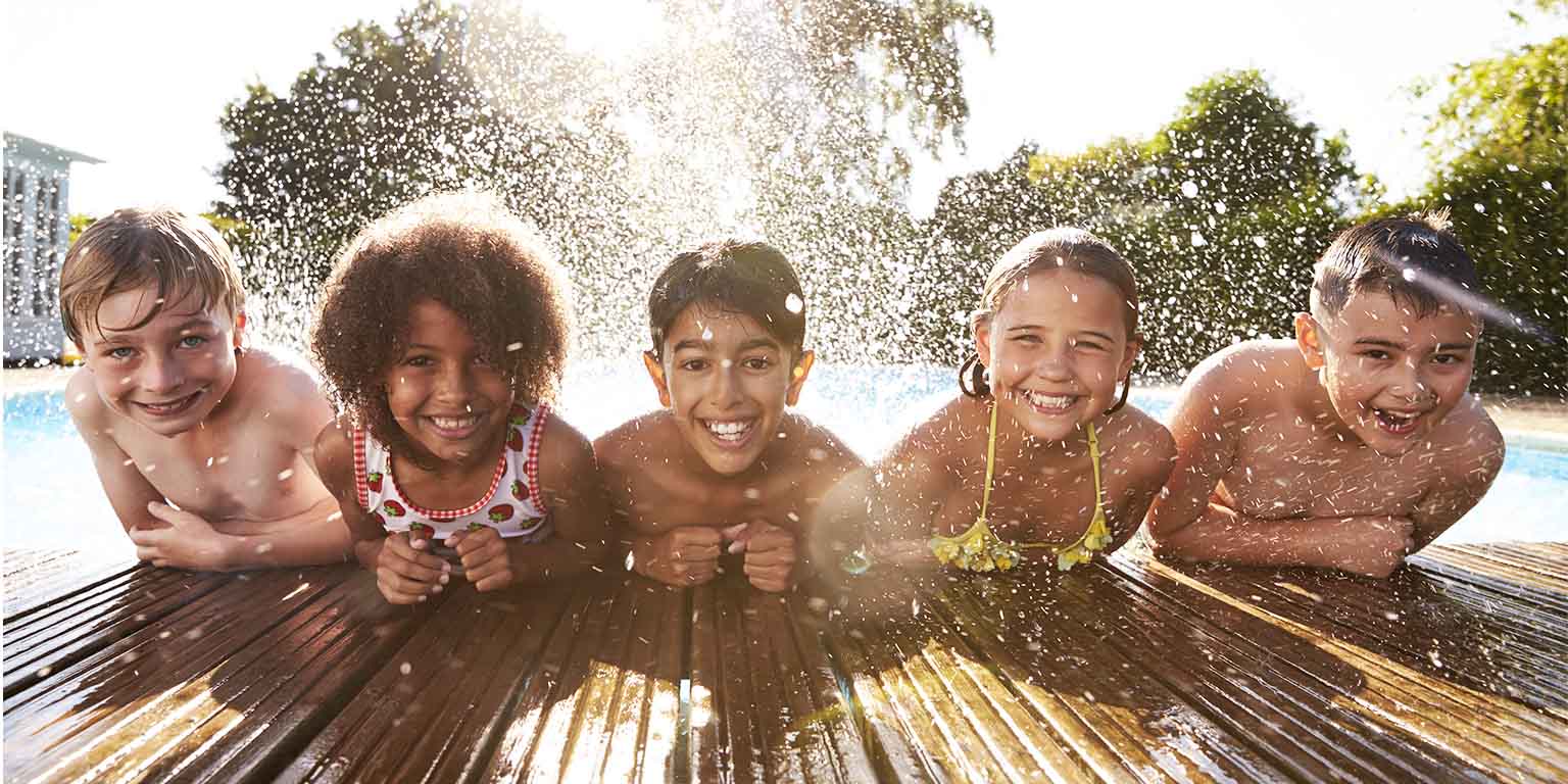 Portrait of five children leaning over the edge of a swimming pool and kicking up water behind them