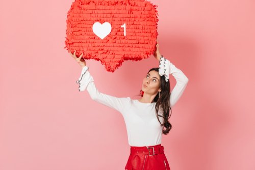 girl holding up instagram like icon on pink background